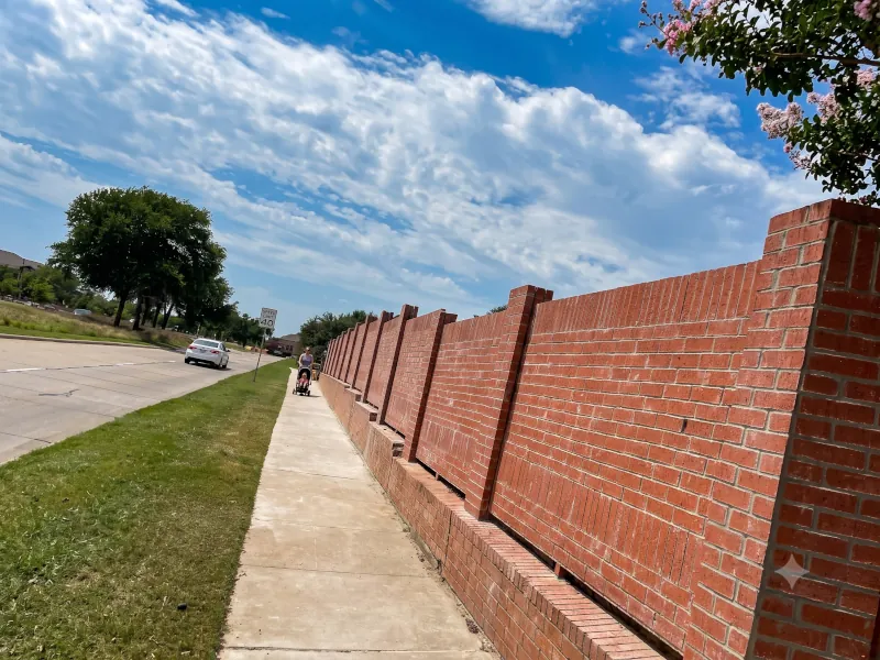 Extended red brick privacy wall along sidewalk with stepped pillar design